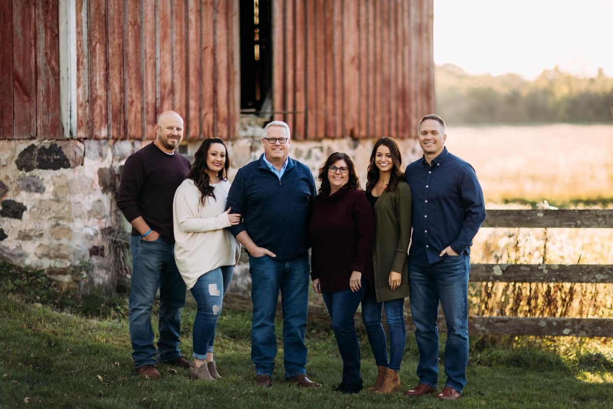 Kim and family posing for a family photo in front of a red barn and wood fence