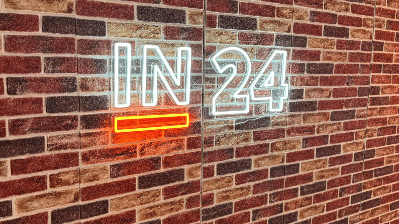 Brick wall with neon sign that says IN24 with orange underline beneath the IN.