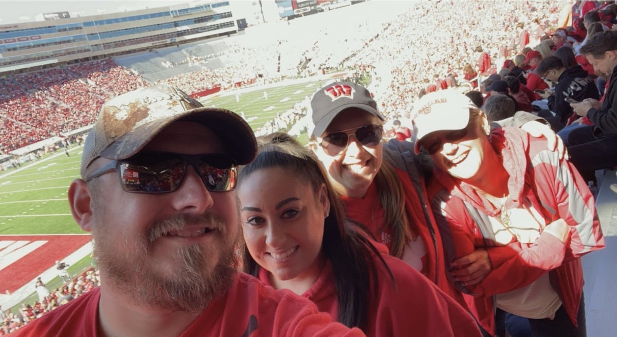 Four people posing for a photo at the Wisconsin Badger's football stadium while watching the game