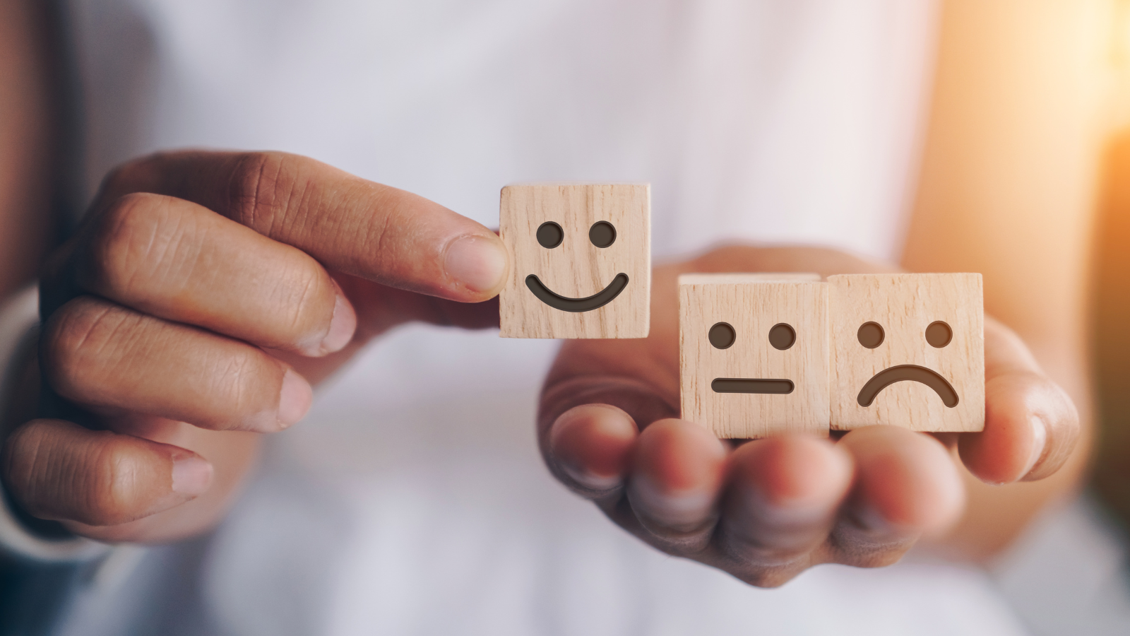 close up of hands holding up tiles with smiley, frown, and strait lipped faces
